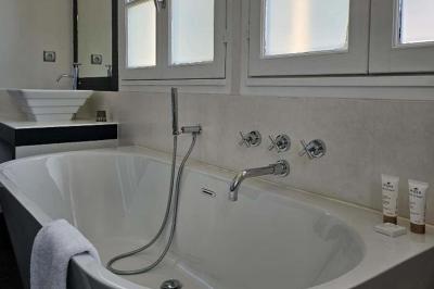 Salle de bain avec baignoire blanche, robinetterie moderne, vasque en arrière-plan et produits de toilette posés.