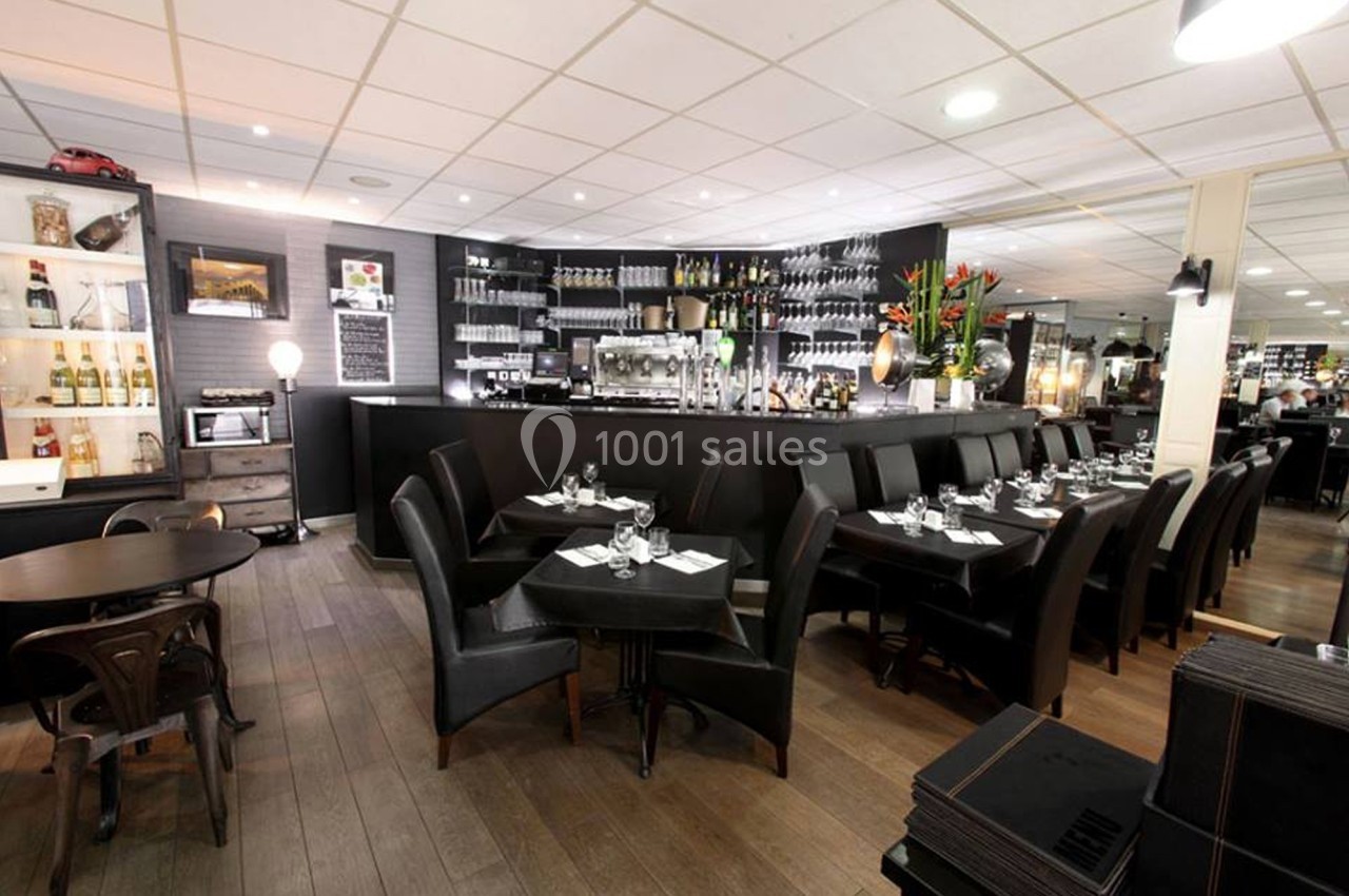 Salle de restaurant moderne avec tables dressées, chaises en cuir noir et un bar en arrière-plan.