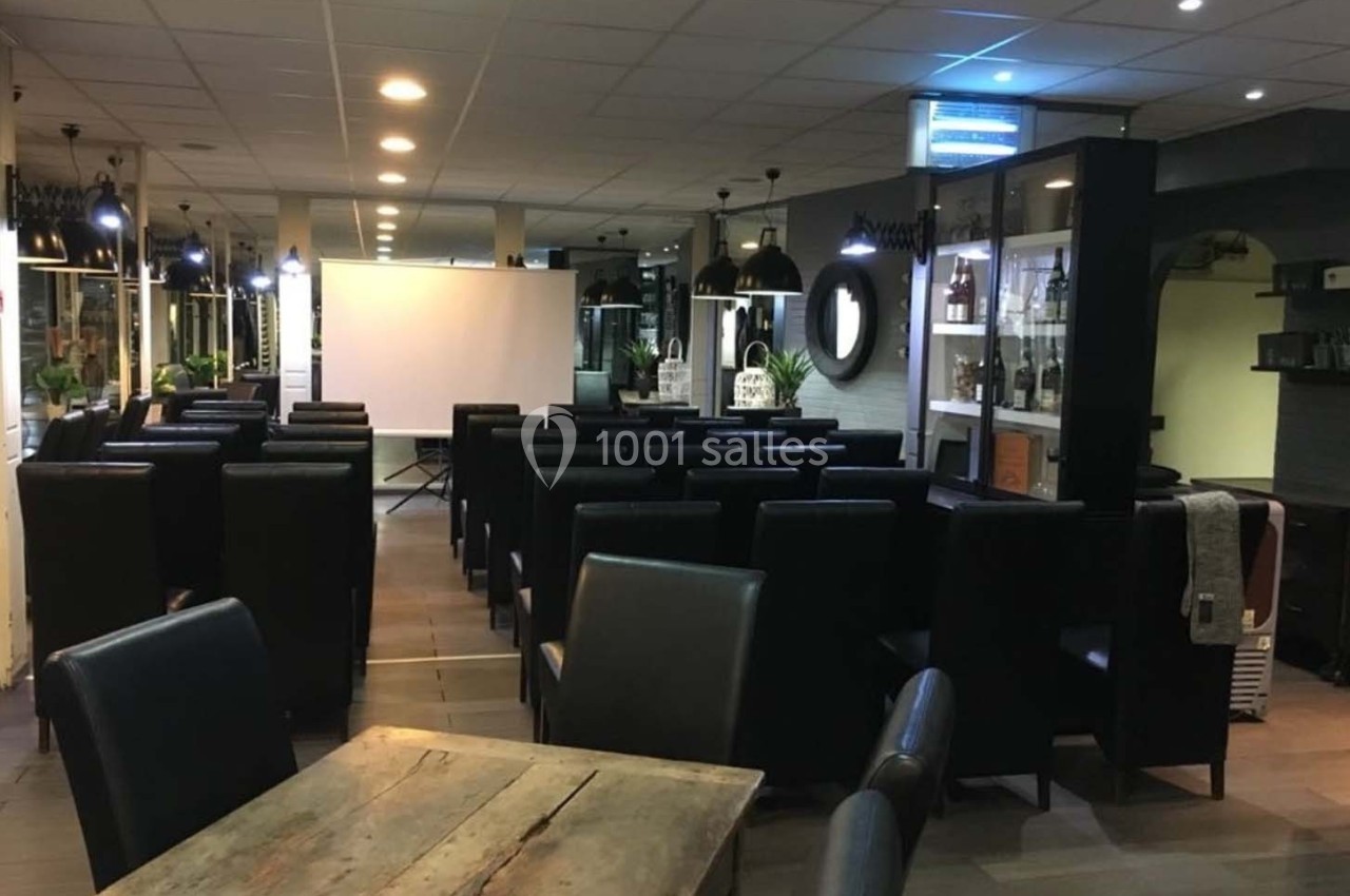 Salle aménagée avec des fauteuils noirs disposés face à un écran de projection, éclairée par des lumières suspendues.