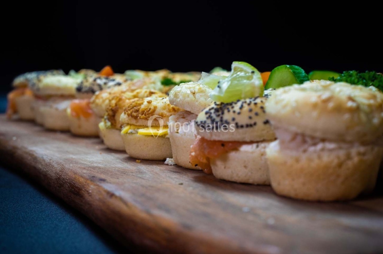 Plateau de petits sandwichs variés garnis de saumon, légumes et fromage, disposés sur une planche en bois.