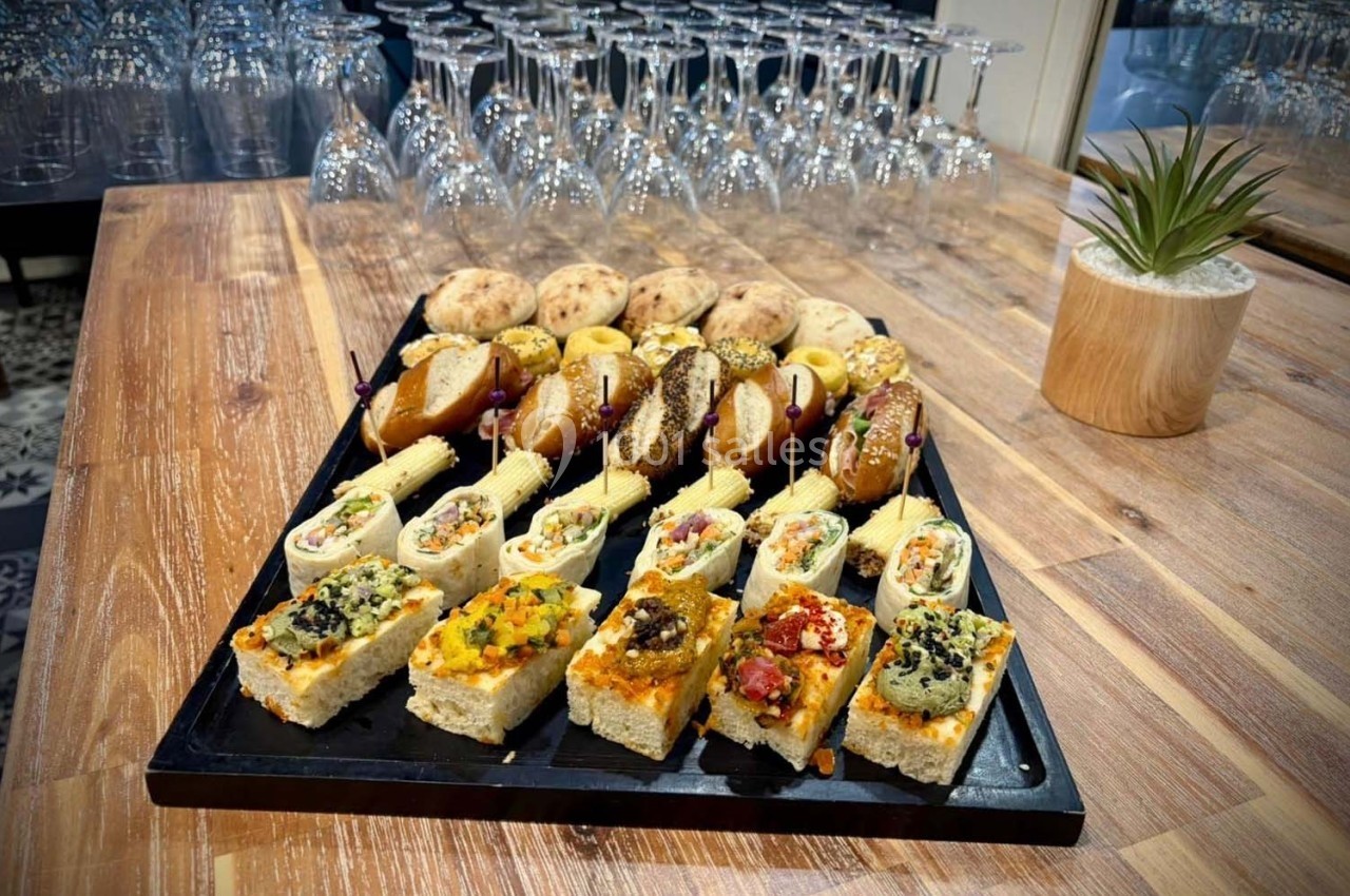 Plateau de canapés variés et pains garnis disposés sur une table en bois, avec des verres à pied en arrière-plan.