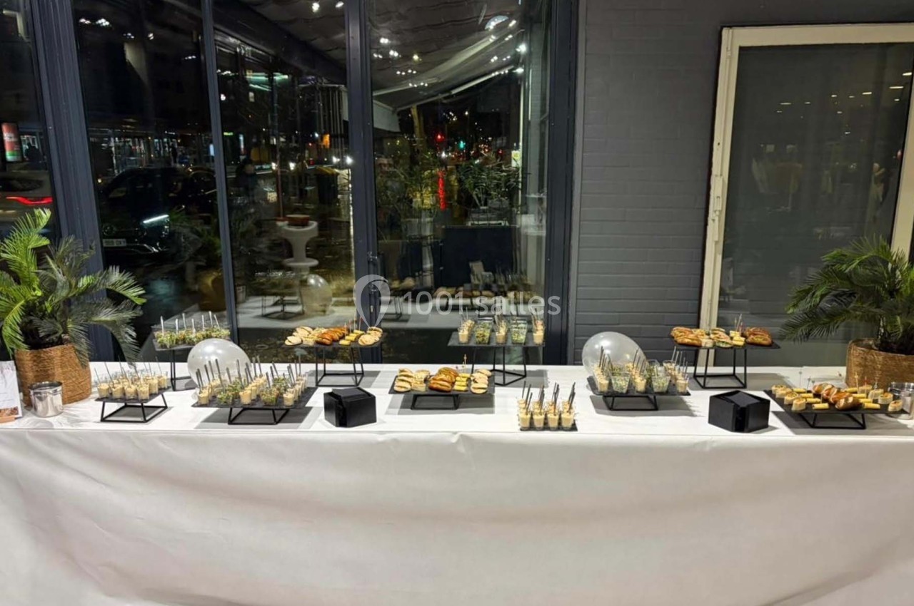 Buffet de réception avec verrines, amuse-bouches et décorations végétales, installé devant une grande baie vitrée.