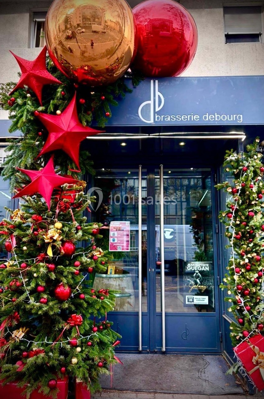 Façade d'une brasserie décorée pour Noël avec sapins, guirlandes lumineuses et grandes boules rouges et dorées.