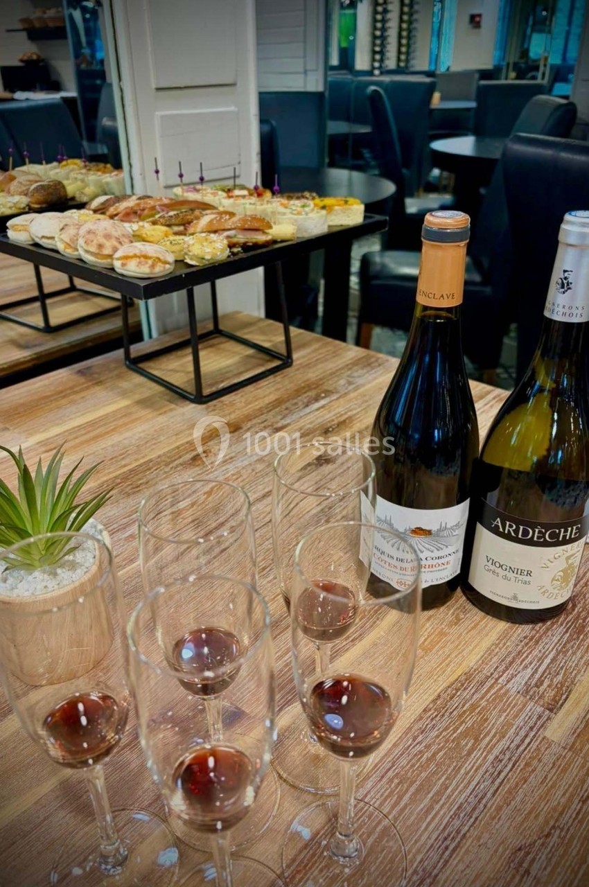 Bouteilles de vin, verres partiellement remplis et plateau de viennoiseries sur une table en bois dans un espace intérieur.