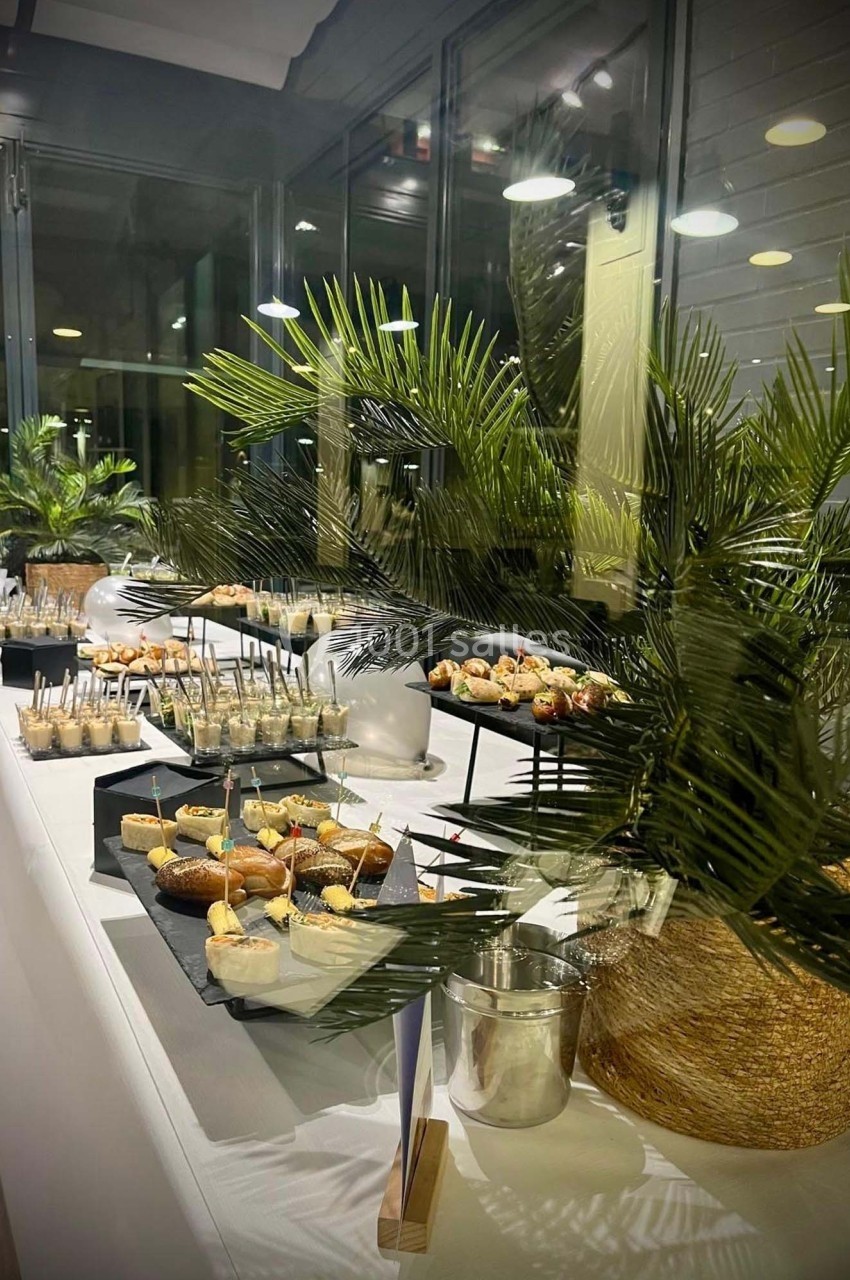 Table garnie de desserts variés présentés sur des plateaux noirs, entourée de plantes décoratives en intérieur.