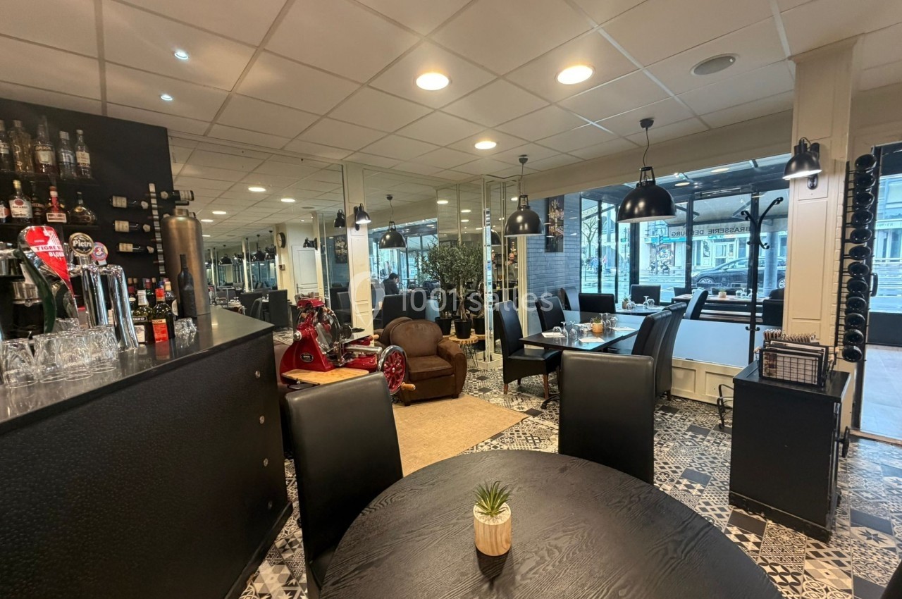 Intérieur d'un restaurant avec un bar, des tables noires, un sol en carreaux et une décoration moderne.