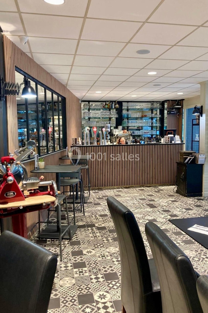 Intérieur d'un restaurant avec un bar en bois, une trancheuse rouge et un sol en carreaux de ciment.