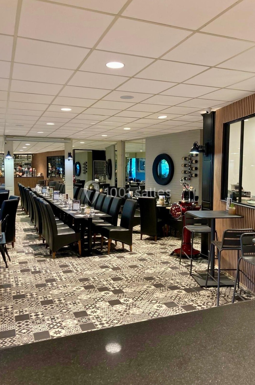 Salle de restaurant moderne avec tables alignées, chaises noires et sol en carreaux à motifs géométriques.