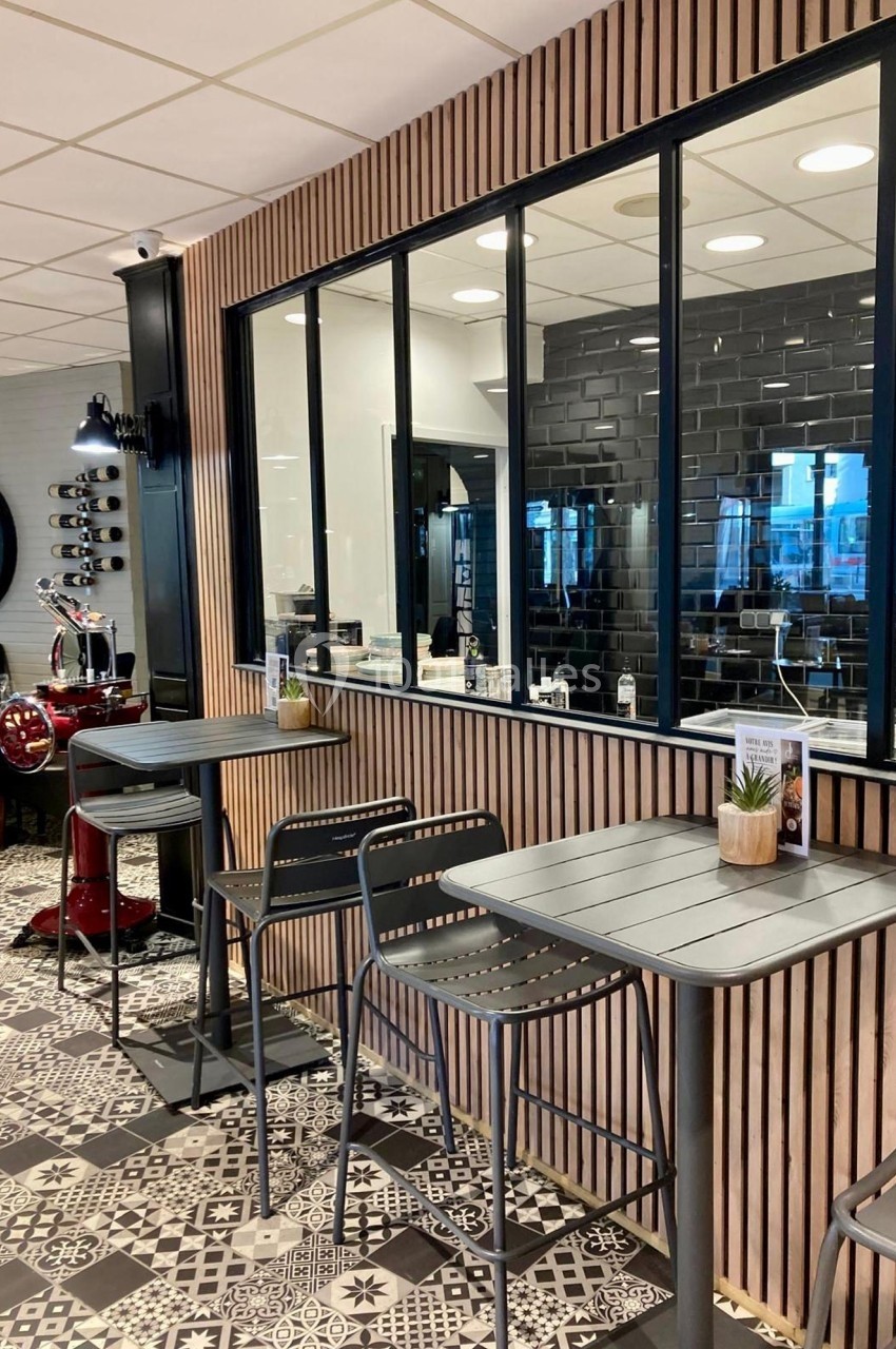 Espace intérieur avec tables hautes, chaises, cloison vitrée et décoration moderne en bois et carrelage noir et blanc.