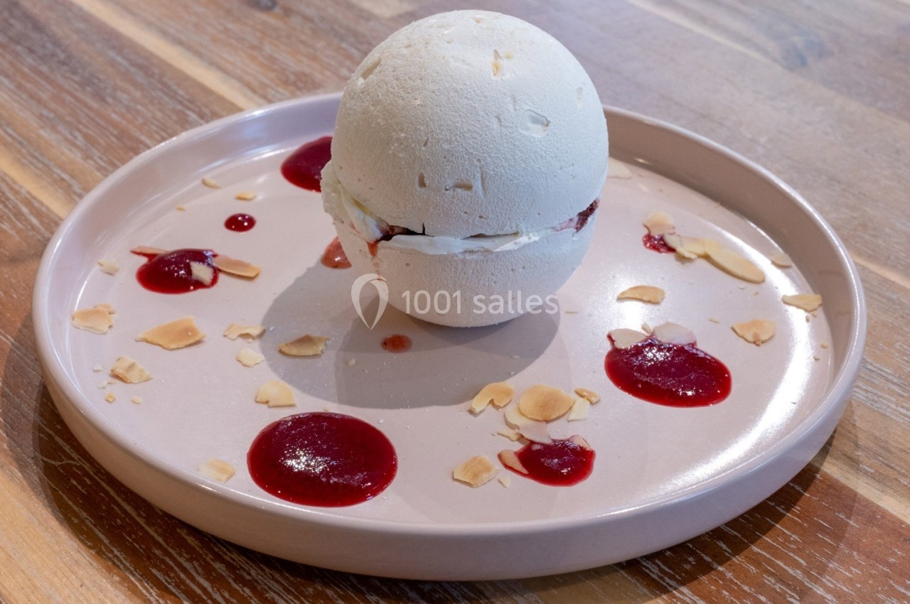 Dessert sphérique en meringue garni de crème et fruits rouges, présenté sur une assiette avec coulis et éclats d'amandes.