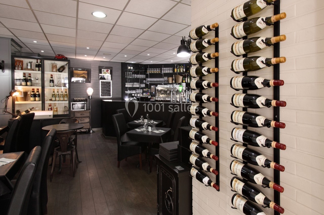 Mur de bouteilles de vin dans un restaurant avec tables dressées et un bar en arrière-plan.