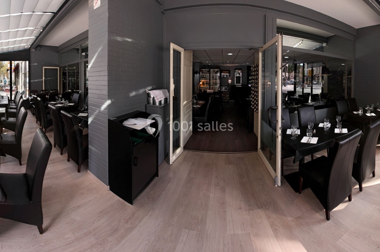 Salle de restaurant lumineuse avec tables dressées, chaises noires et grandes baies vitrées donnant sur l'extérieur.