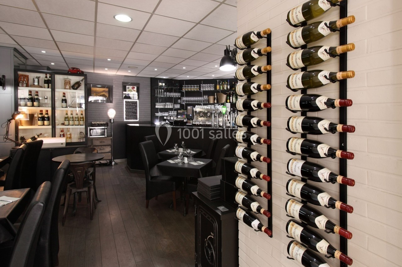 Mur de bouteilles de vin dans un restaurant avec tables dressées et bar en arrière-plan.