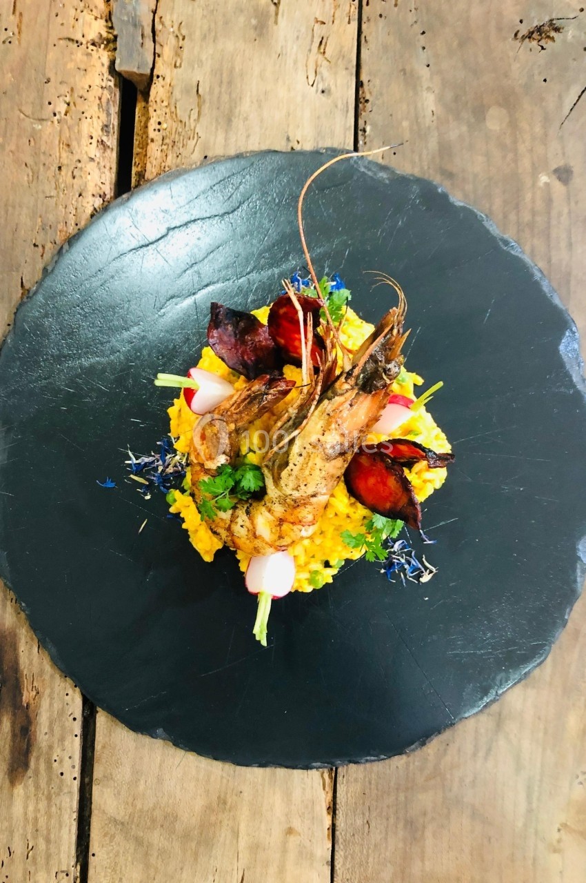 Assiette de risotto au safran avec crevettes grillées, légumes colorés et herbes, présentée sur une ardoise noire.