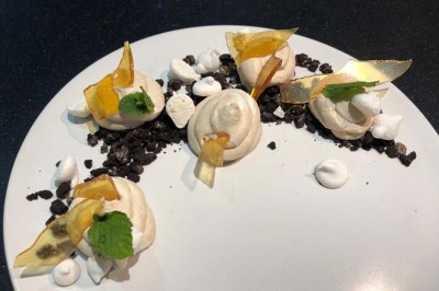 Assiette de dessert composée de meringues, éclats de caramel, feuilles de menthe et miettes de biscuit noir.