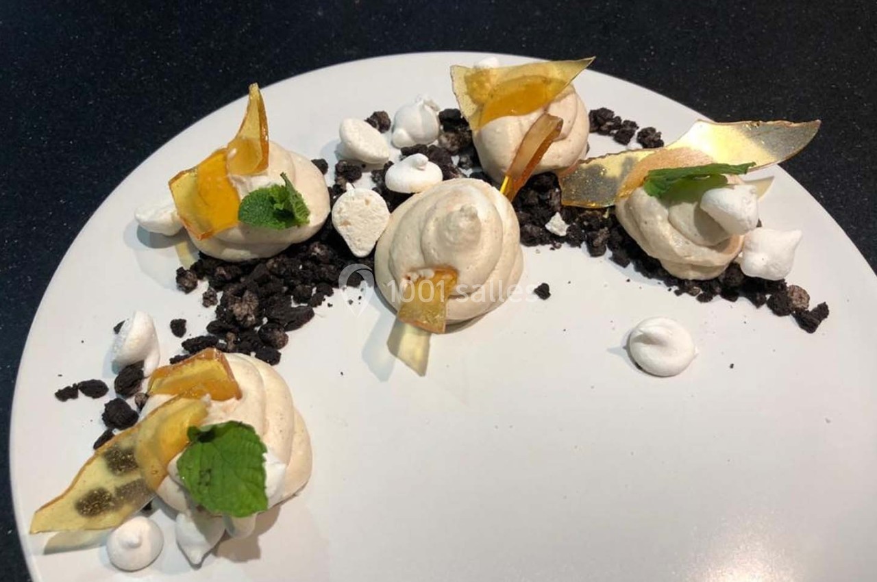 Assiette de dessert composée de meringues, éclats de caramel, feuilles de menthe et miettes de biscuit noir.