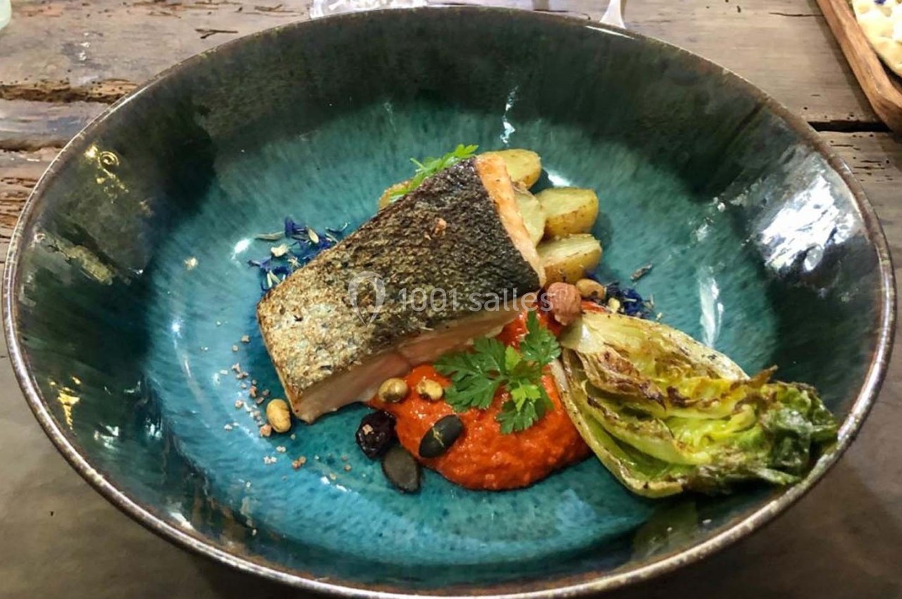 Assiette contenant un filet de saumon grillé, légumes rôtis, purée rouge et herbes fraîches, servie dans un bol bleu.