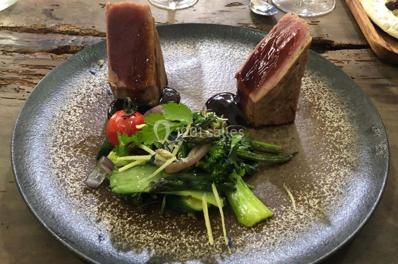 Assiette gastronomique avec deux morceaux de viande saignante, légumes verts, tomate cerise et sauce.