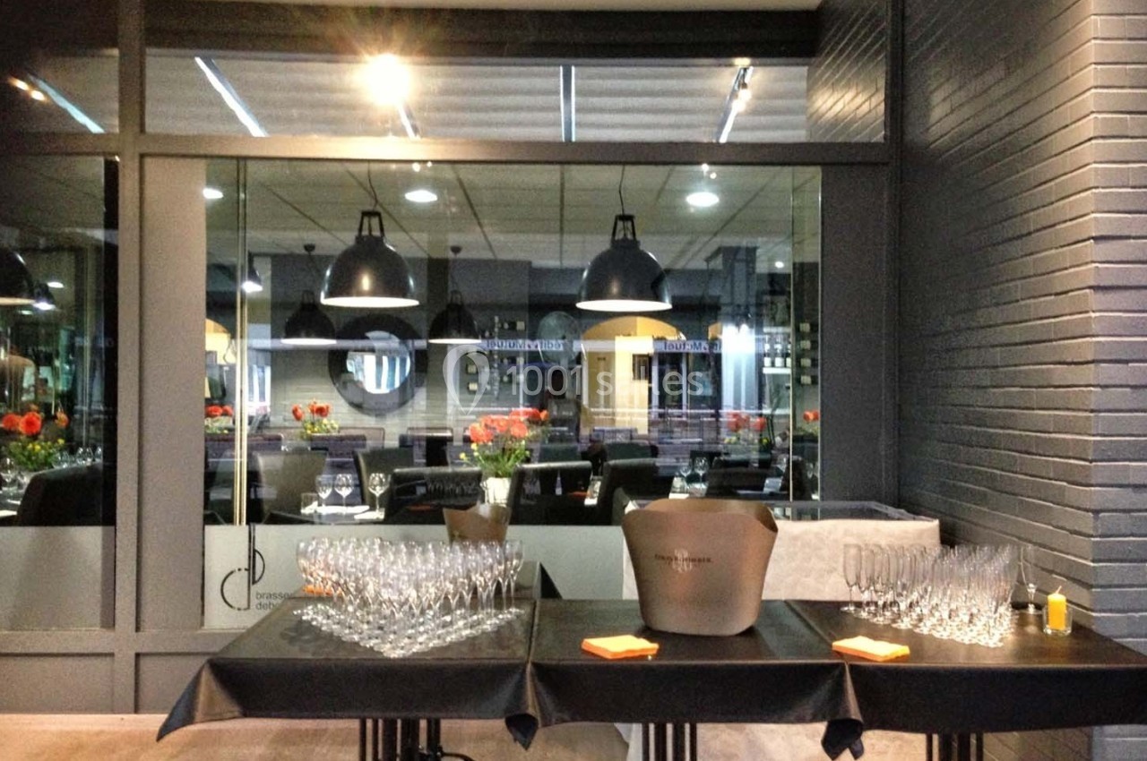 Terrasse d'un restaurant avec tables dressées, verres à pied alignés et vue sur une salle intérieure éclairée.