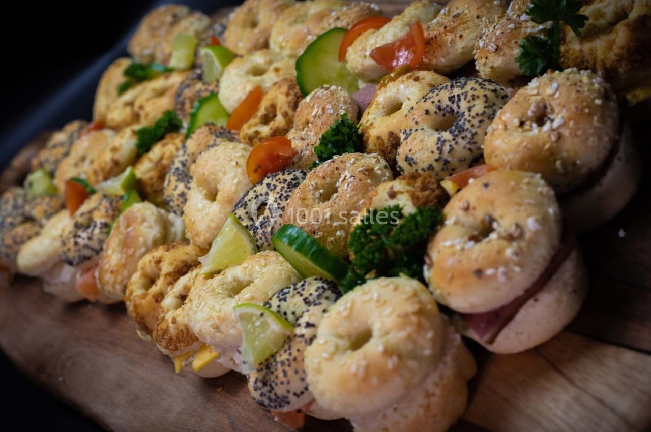 Plateau de mini-bagels garnis de légumes, fromage et charcuterie, disposés sur une planche en bois.