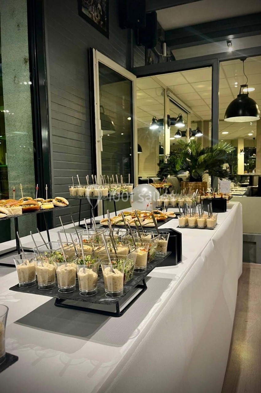 Buffet de verrines et amuse-bouches disposés sur une table blanche dans un espace intérieur moderne.