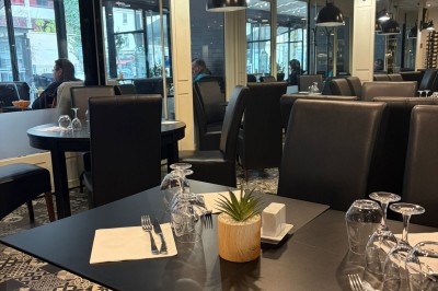 Salle de restaurant avec une table dressée près d'une baie vitrée donnant sur une rue urbaine sous la pluie.