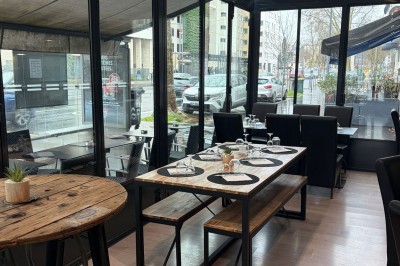 Salle de restaurant avec une table dressée près d'une baie vitrée donnant sur une rue urbaine sous la pluie.