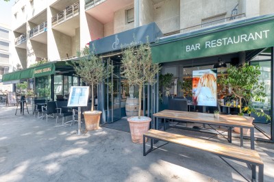 Miniature Location salle Lyon 7 (Rhône) - Brasserie Debourg #60 Comptoir de bar moderne avec revêtement en bois, étagères de bouteilles, tables hautes et décoration végétale.