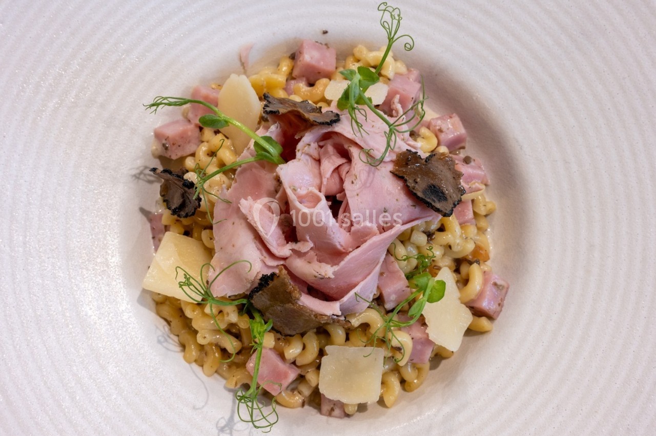 Assiette de pâtes aux dés de jambon, copeaux de parmesan, truffes et herbes fraîches, servie dans un plat blanc.