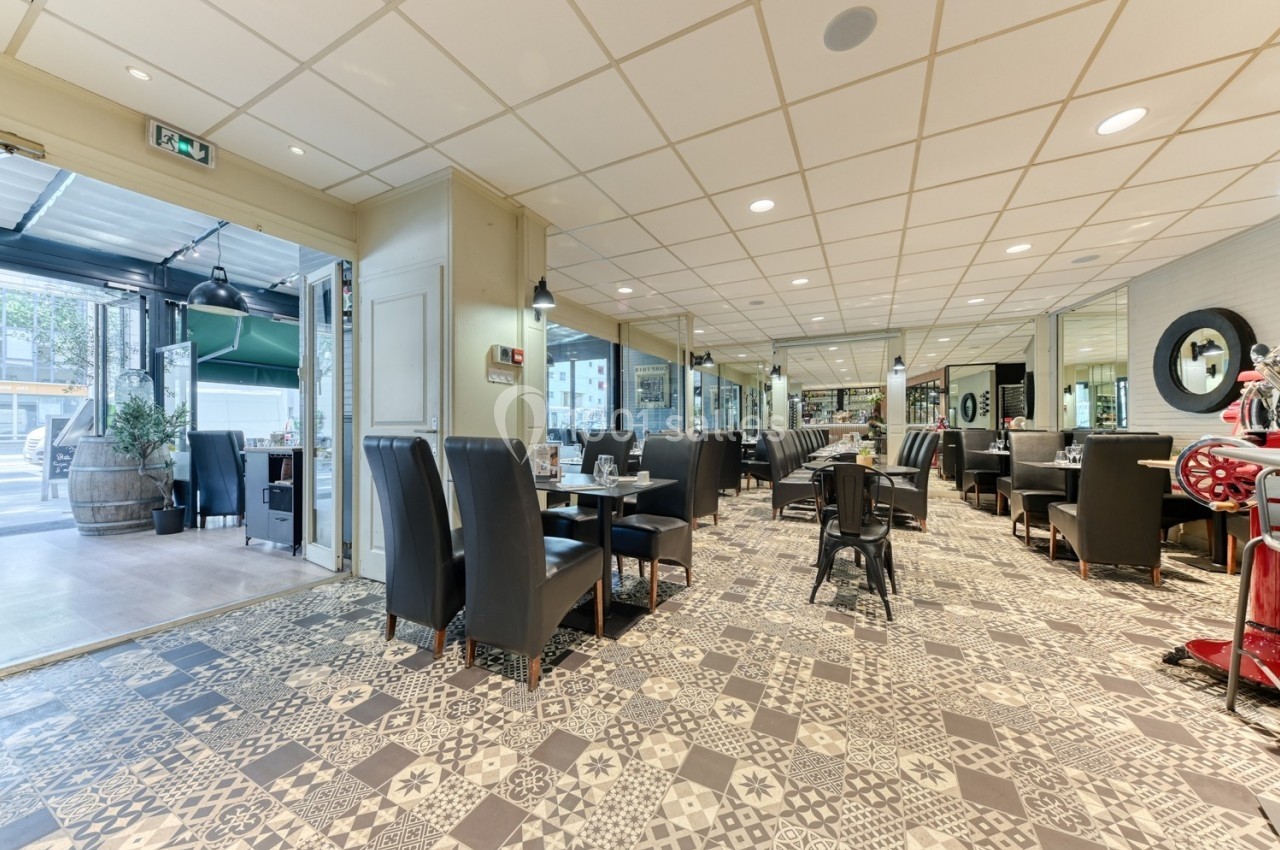 Salle de restaurant lumineuse avec tables dressées, chaises noires et sol en carreaux de ciment décoratifs.
