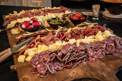 Buffet avec paniers de pain, légumes frais, brochettes et autres plats disposés sur une table dans un cadre intérieur.
