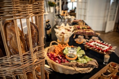 Buffet avec paniers de pain, légumes frais, brochettes et autres plats disposés sur une table dans un cadre intérieur.
