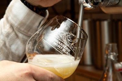 Fondue au fromage dans un caquelon rouge avec des morceaux de pain trempés, accompagnée de vin et de cornichons.