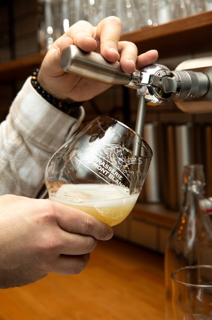 Une main sert une bière blonde à la pression dans un verre marqué ’Brasserie du Mont-Blanc’.
