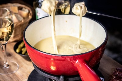 Fondue au fromage dans un caquelon rouge avec des morceaux de pain trempés, accompagnée de vin et de cornichons.