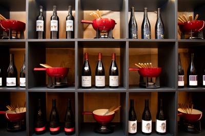 Fondue au fromage dans un caquelon rouge avec des morceaux de pain trempés, accompagnée de vin et de cornichons.