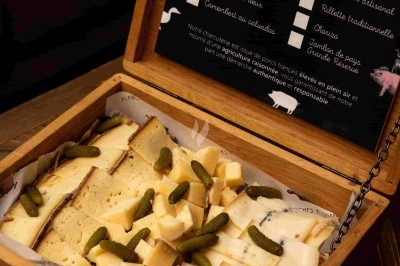 Assortiment de fromages coupés en morceaux, accompagné de cornichons, présenté dans une boîte en bois ouverte.