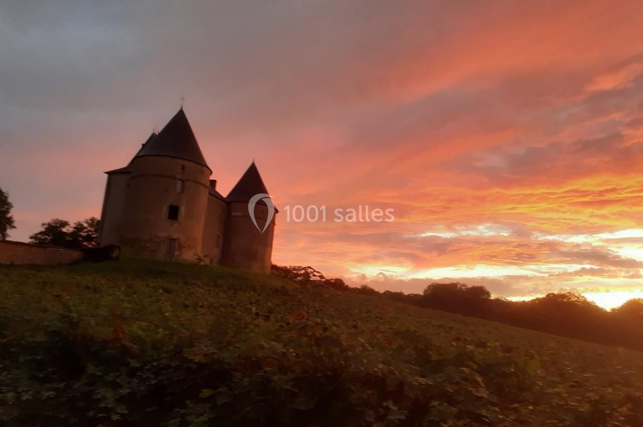 Château ancien à deux tours sur une colline, entouré de végétation, sous un ciel de coucher de soleil coloré.