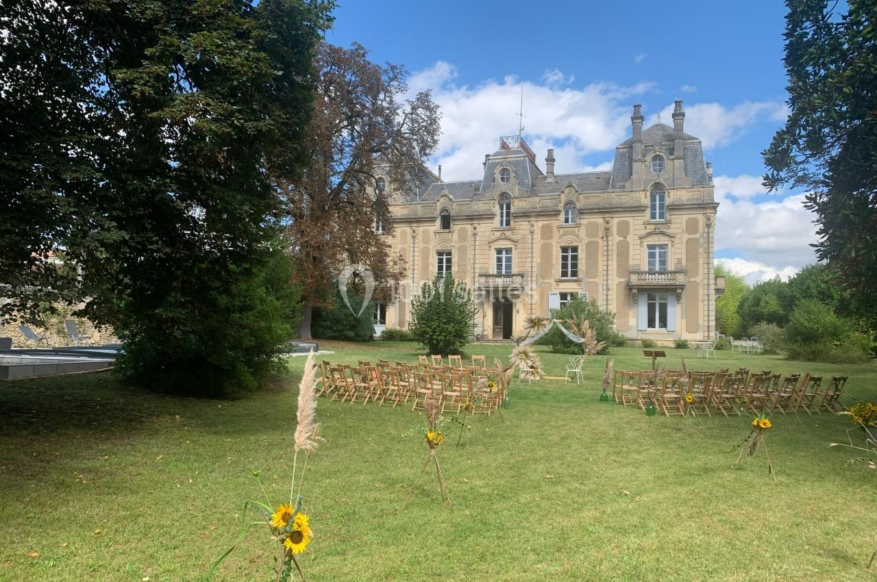 Château en pierre entouré de verdure avec des chaises disposées pour une cérémonie en plein air.