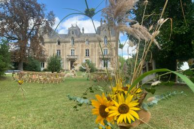 Salle de réception décorée avec des tables dressées, nappes blanches, bouquets de roses et chaises blanches.