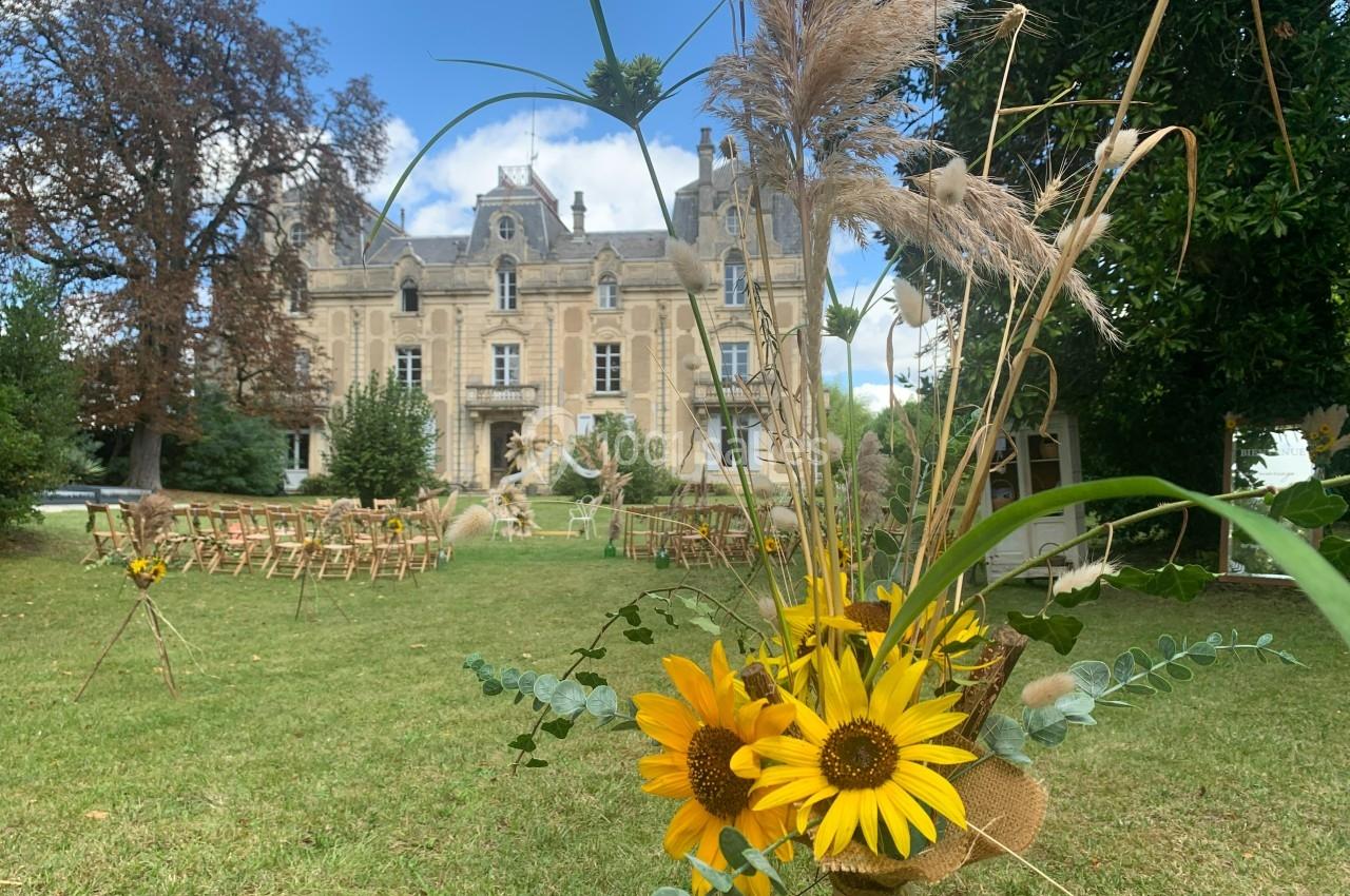 Décoration florale avec tournesols au premier plan, devant un château entouré de verdure et de chaises disposées en…