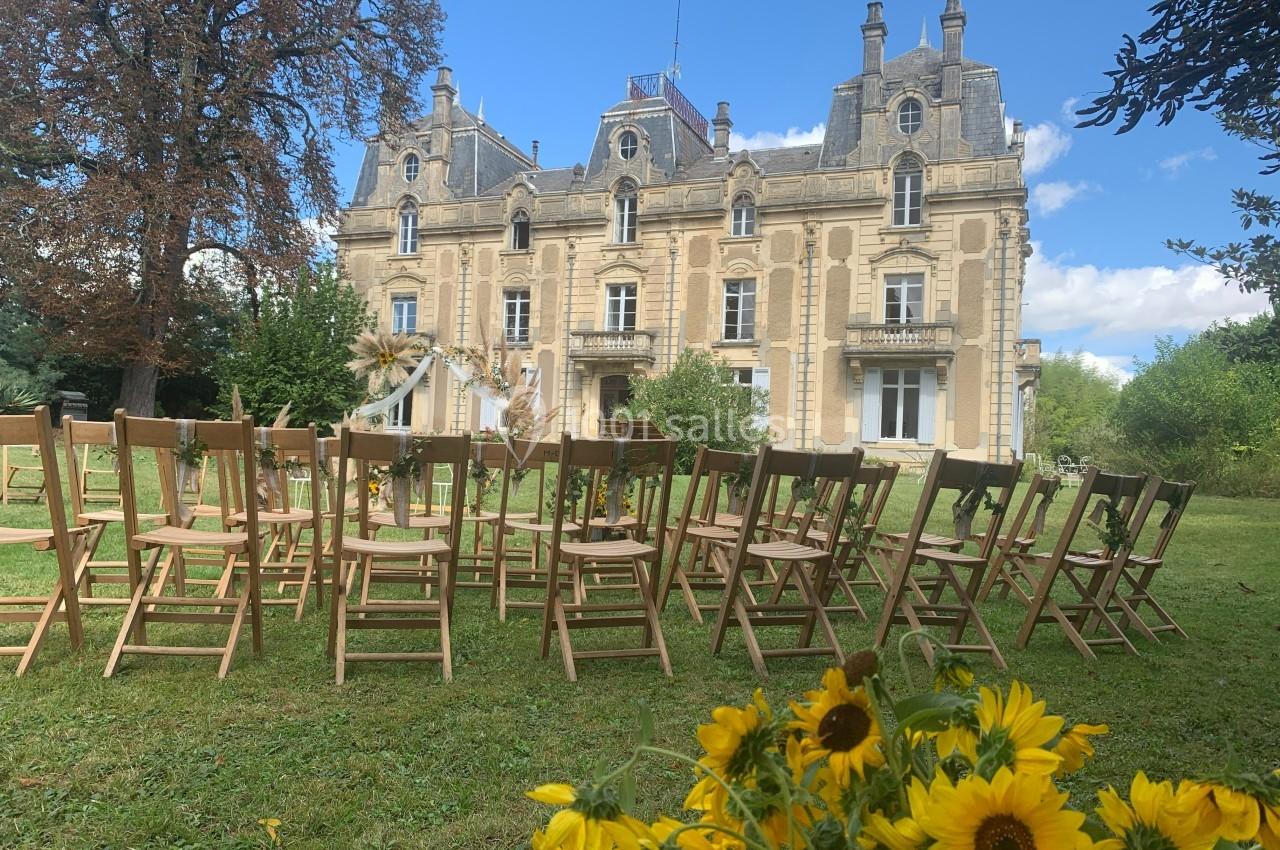 Chaises en bois disposées en extérieur devant un château, avec des tournesols en premier plan.