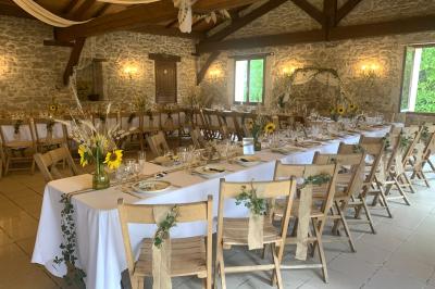 Salle de réception décorée avec des tables dressées, nappes blanches, bouquets de roses et chaises blanches.