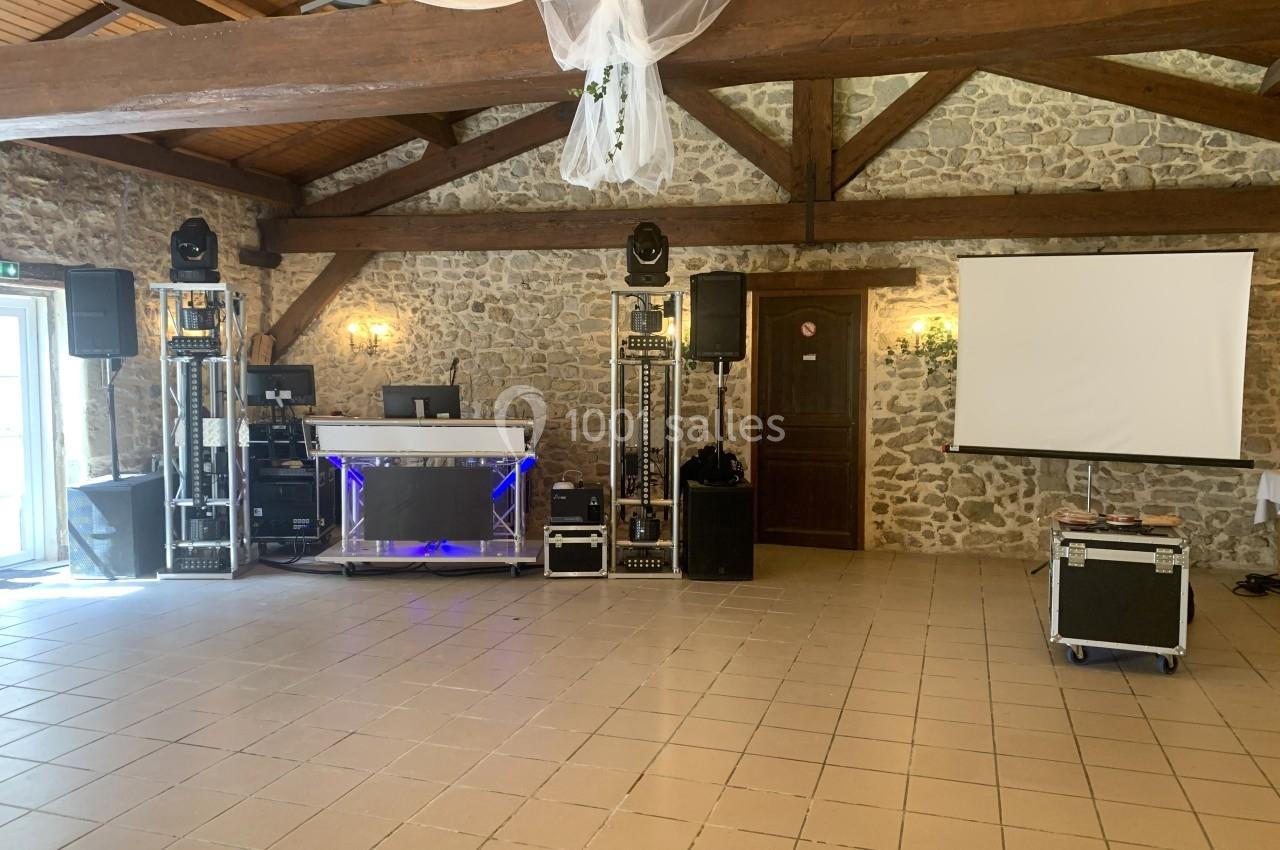 Salle de réception avec murs en pierre, équipements audio-visuels, piste de danse et écran de projection.