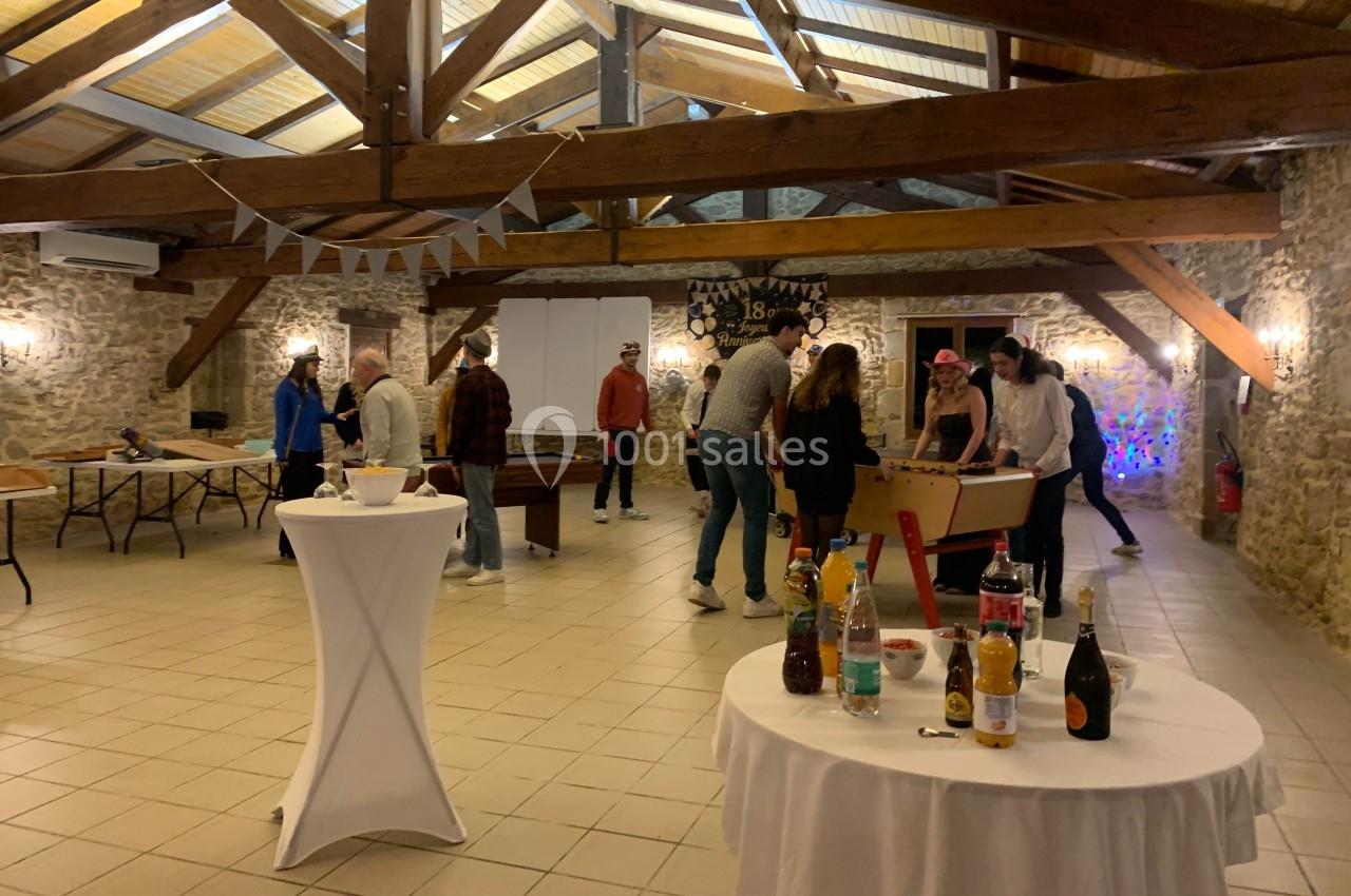 Des personnes jouent et discutent dans une salle en pierre avec charpente apparente, décorée pour un événement.
