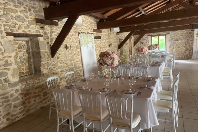 Salle de réception décorée avec des tables dressées, nappes blanches, bouquets de roses et chaises blanches.