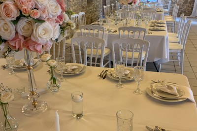 Salle de réception décorée avec des tables dressées, nappes blanches, bouquets de roses et chaises blanches.