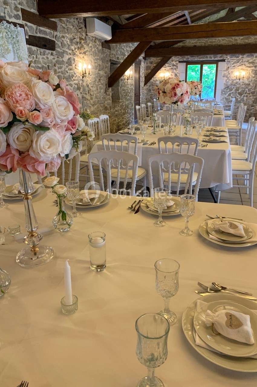 Salle de réception décorée avec des tables dressées, nappes blanches, bouquets de roses et chaises blanches.