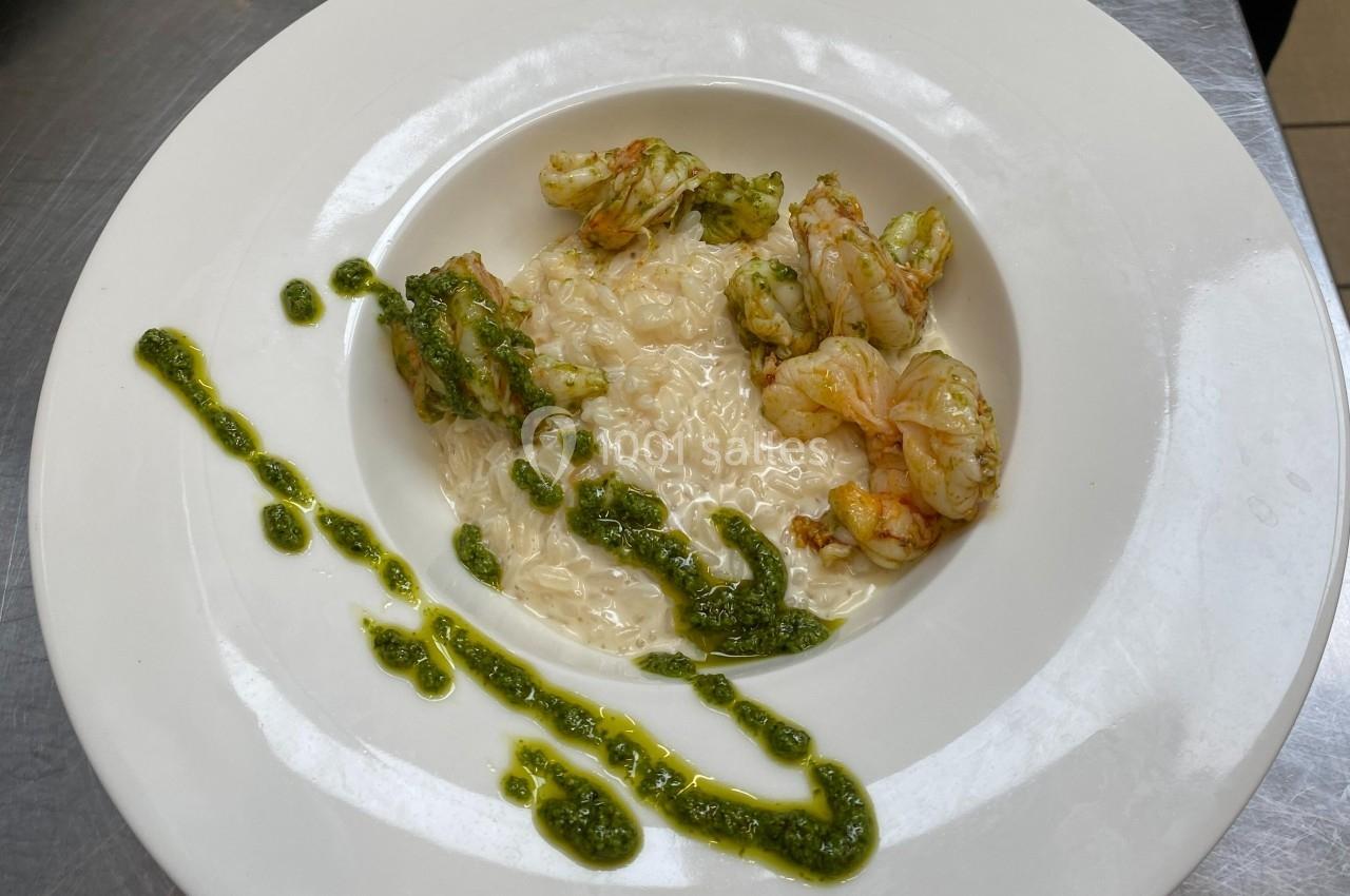 Assiette de risotto crémeux accompagné de crevettes et décorée de sauce verte disposée en filet.