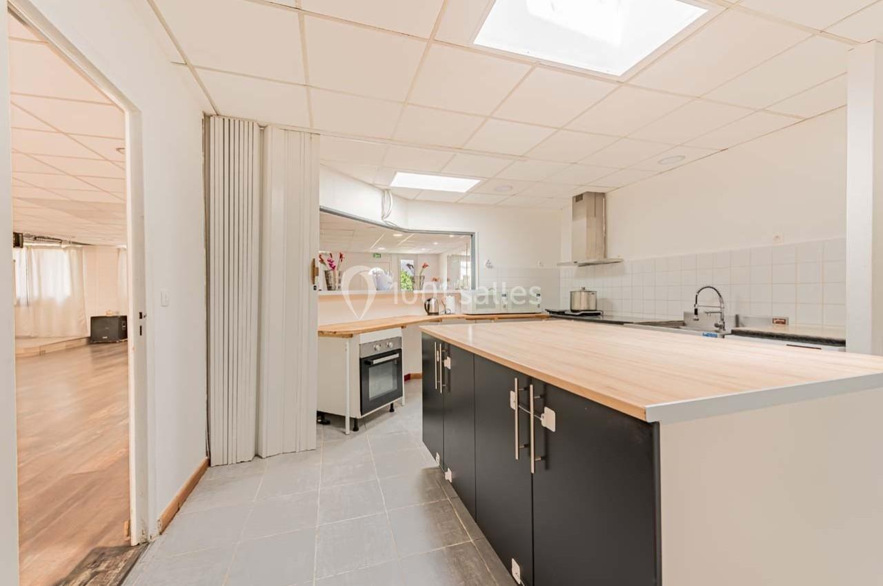 Cuisine moderne avec îlot central en bois, meubles noirs, carrelage gris et lumière naturelle provenant d'une fenêtre de…